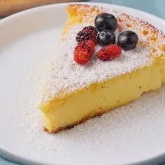 Ein Stück saftiger Quarkkuchen ohne Boden, bestäubt mit Puderzucker und garniert mit frischen Beeren.
