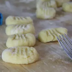 Frisch geformte Gnocchi liegen auf bemehltem Holz. Eine Gabel und ein blauer Lappen deuten darauf hin, dass das Gnocchi selber machen gerade erst begonnen hat.