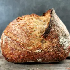 Ein rustikales Brot mit knuspriger Kruste liegt auf Holzbrettern. Schade, dass das Brot beim Backen nicht aufgegangen ist, aber es sieht trotzdem lecker aus.