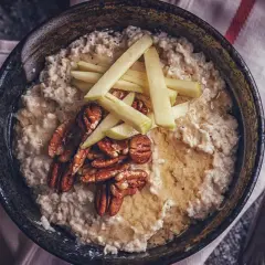 Schüssel mit cremigem Haferbrei, garniert mit Apfelspalten, Pekannüssen und Honig. Ein einfaches und leckeres Haferbrei Rezept für den Morgen.