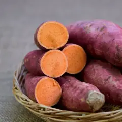 Ein Korb voller tropischer Süßkartoffeln, einige ganz, andere aufgeschnitten, enthüllt ihr leuchtend orangefarbenes Inneres.