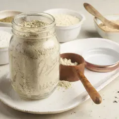 Glas gefüllt mit selbstgemachtem Proteinpulver, daneben Schüsseln mit Zutaten. Perfekt für dein Proteinshake-Rezept!