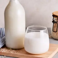 Frisch zubereitete Reismilch in einer Flasche und einem Glas, daneben Reis in einem Glasbehälter. So einfach ist es, Reismilch selber machen.