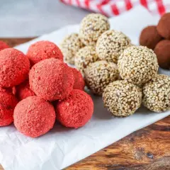 Leckeres Power Balls Rezept: Rote Erdbeer-Bällchen, Sesam-Bällchen und schokoladige Trüffel auf einem Holzbrett.