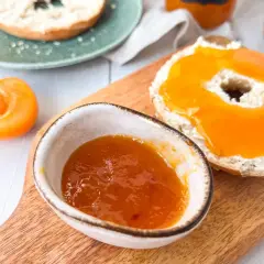 Ein Bagel mit Frischkäse und leckerer Aprikosenmarmelade, die Lust auf das Aprikosenmarmelade Rezept macht. Daneben eine halbe Aprikose.