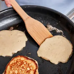 Buttermilch pancakes bräunen in der Pfanne, eine Holzspachtel wendet sie.