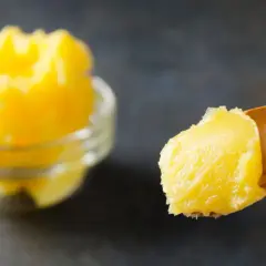 Goldgelbe, cremige vegane Butter auf einem Holzlöffel, daneben eine Schüssel voll. Perfekt, um vegane Butter selber machen zu können.