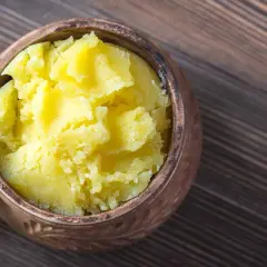 Ein Topf mit selbstgemachtem Ghee auf einem Holztisch. Das goldgelbe, cremige Ghee ist bereit zum Kochen.