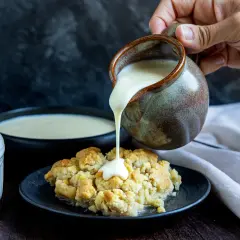 Vanillesauce selber machen: Ein goldbrauner Crumble wird mit cremiger Vanillesauce aus einem Krug übergossen.