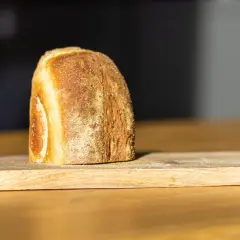 Ein frisch gebackenes Brot liegt auf einem Holzbrett. Die Kruste ist goldbraun und knusprig, was zeigt, wie wird brot saftig.