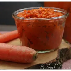 Ein Glas mit leckerer Karotten Marmelade, daneben frische Karotten.