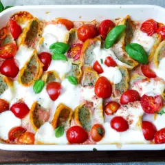 Herzhafter Maultaschen Auflauf mit Kirschtomaten und geschmolzenem Mozzarella, garniert mit frischem Basilikum.