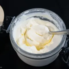 Creme fraiche selber machen ist einfach! Ein Löffel nimmt eine Portion der cremigen Masse aus dem Glas.