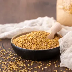 Schale mit goldenen Leinsamen und Holzschaufel, daneben ein Papiersack. Der Unterschied zwischen Leinsamen und Goldleinsamen wird hier visuell dargestellt.
