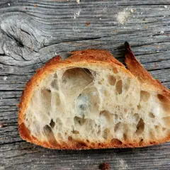 Ein Stück **selbstgebackenes Brot zu fest** mit großer Krume und knuspriger Kruste liegt auf einer alten Holzoberfläche.