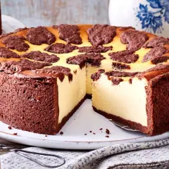 Ein saftiger russischer Zupfkuchen mit Schokoladenboden und cremiger Käsemasse, dekoriert mit dunklen Schokoladenstückchen.