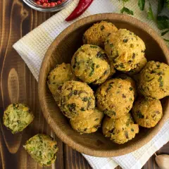 Schüssel mit frittierten Falafel-Bällchen, die aus frischen falafel zutaten zubereitet wurden. Daneben liegen Knoblauch und Kräuter.
