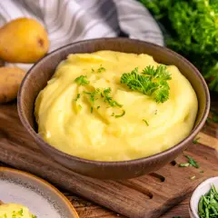 Cremiger Kartoffelbrei, garniert mit Petersilie, ist bereit für ein köstliches Kartoffelbrei Rezept. Frische Kartoffeln, Milch und Kräuter liegen bereit.