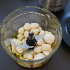 Ein Glas-Zerkleinerer mit vielen geschälten Knoblauchzehen und etwas Öl. Perfekt für ein schnelles Knoblauchpaste Rezept.