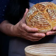Hände halten ein frisch gebackenes Sauerteigbrot, das gerade aus dem Gärkorb genommen wurde. Der Teig ist perfekt aufgegangen.