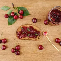 Frisches Brot mit Kirschmarmelade, garniert mit Minze. Ein Glas Kirschmarmelade und frische Kirschen daneben. Perfekt für ein Kirschmarmelade Rezept.