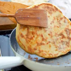 Ein goldbraunes Pfannenbrot wird mit einem Holzspatel in einer Pfanne gewendet. Perfekt für ein einfaches Pfannenbrot Rezept.