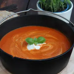 Ein köstliches Tomatensuppe Rezept mit frischen Tomaten, garniert mit Basilikum und einem Klecks Sahne, serviert in einem Gusseisentopf mit Brot.