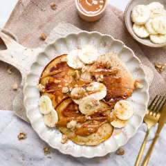 Bananen Pancakes ohne Ei, garniert mit Bananenscheiben, Walnüssen und einer cremigen Sauce. Ein köstlicher Start in den Tag.