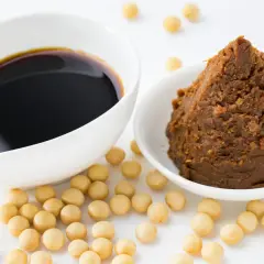 Miso-Paste und Sojasauce in weißen Schalen, umgeben von Sojabohnen. Eine köstliche Alternative zu Hefeflocken für herzhafte Gerichte.