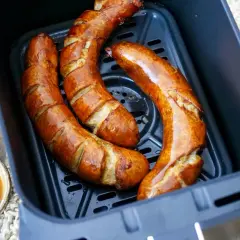 Drei goldbraune Bratwürste in der Heißluftfritteuse, bereit für leckere Bratwurst Rezepte. Dazu ein Schälchen mit Sauce und frische Petersilie.