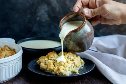 Vanillesauce selber machen: Ein goldbrauner Crumble wird mit cremiger Vanillesauce aus einem Krug übergossen.