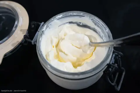 Creme fraiche selber machen ist einfach! Ein Löffel nimmt eine Portion der cremigen Masse aus dem Glas.