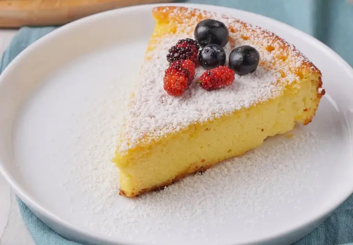 Ein Stück saftiger Quarkkuchen ohne Boden, bestäubt mit Puderzucker und garniert mit frischen Beeren.