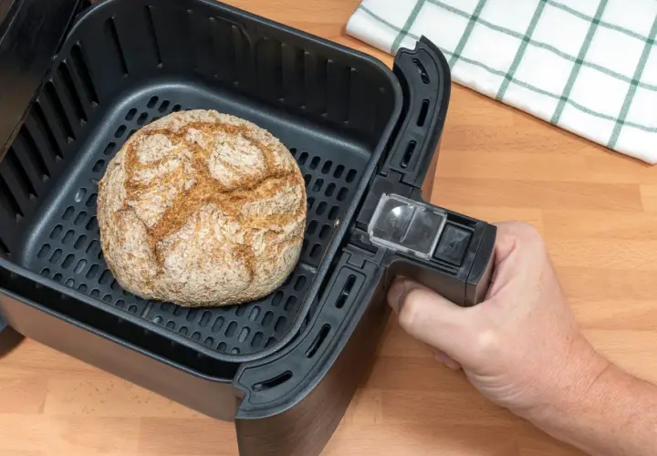 Ein goldbraunes Brot liegt im Korb eines Airfryers. Perfekt zum brot backen im airfryer für knusprigen Genuss.