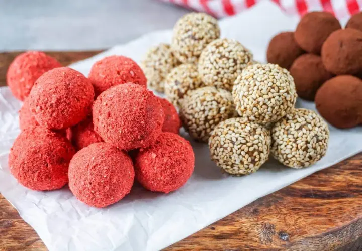 Leckeres Power Balls Rezept: Rote Erdbeer-Bällchen, Sesam-Bällchen und schokoladige Trüffel auf einem Holzbrett.