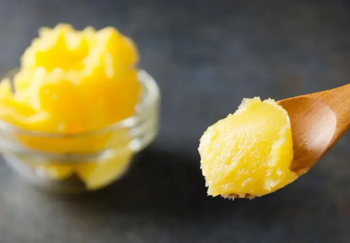 Goldgelbe, cremige vegane Butter auf einem Holzlöffel, daneben eine Schüssel voll. Perfekt, um vegane Butter selber machen zu können.