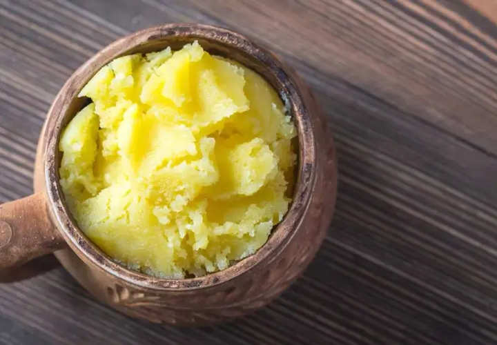 Ein Topf mit selbstgemachtem Ghee auf einem Holztisch. Das goldgelbe, cremige Ghee ist bereit zum Kochen.
