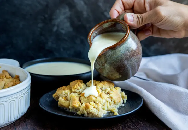 Vanillesauce selber machen: Ein goldbrauner Crumble wird mit cremiger Vanillesauce aus einem Krug übergossen.