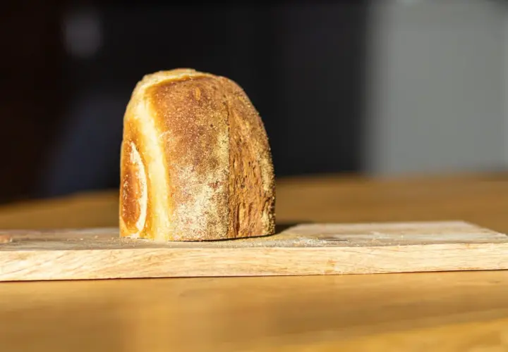Ein frisch gebackenes Brot liegt auf einem Holzbrett. Die Kruste ist goldbraun und knusprig, was zeigt, wie wird brot saftig.