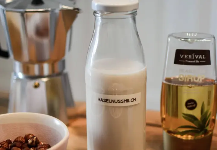 Zutaten für Haselnussmilch selber machen: Haselnüsse, Moka-Kanne, Agavendicksaft und eine Flasche mit selbstgemachter Haselnussmilch.