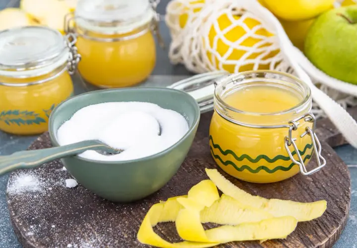 Zutaten für gelierzucker selber machen: Zucker in einer Schüssel, Apfelscheiben, Äpfel und Zitronenschalen.