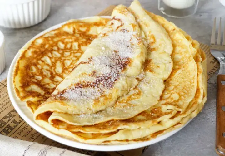 Ein Stapel goldbrauner Pfannkuchen, bestreut mit Zucker. Ein einfaches Pfannkuchen Rezept für jeden Tag.