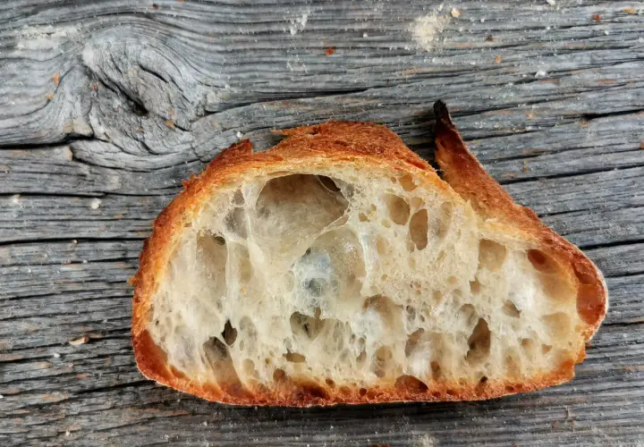 Ein Stück **selbstgebackenes Brot zu fest** mit großer Krume und knuspriger Kruste liegt auf einer alten Holzoberfläche.