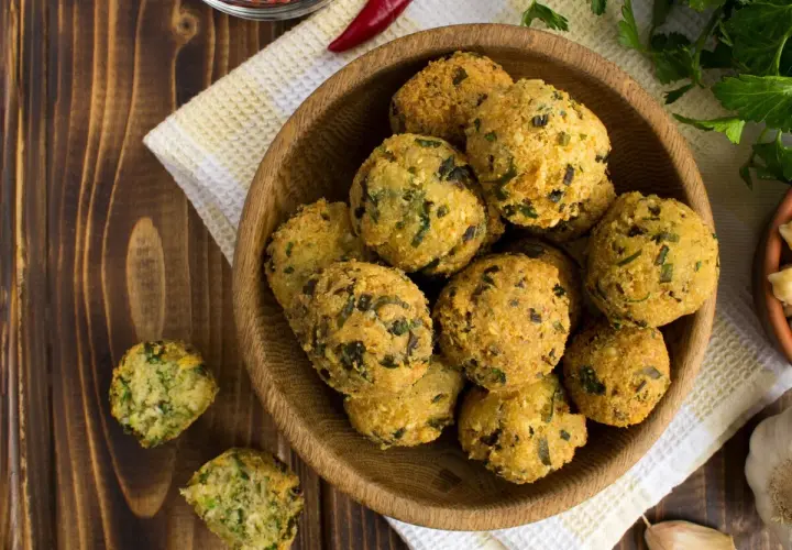 Schüssel mit frittierten Falafel-Bällchen, die aus frischen falafel zutaten zubereitet wurden. Daneben liegen Knoblauch und Kräuter.