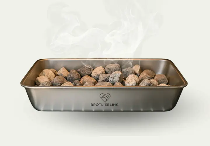 Dampf steigt aus einem Metallbehälter mit Steinen auf. Für knuspriges Brot muss man Wasser in den Ofen geben.
