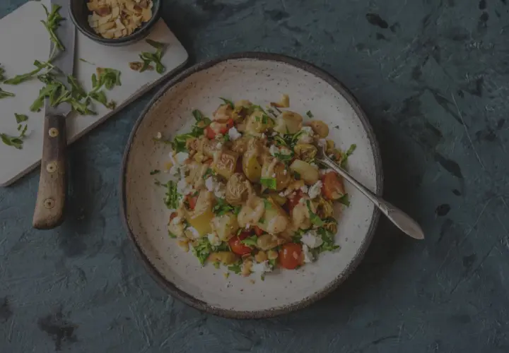 Herzhafter Salat mit bratkartoffeln aus rohen kartoffeln, Feta, Kirschtomaten und Rucola, garniert mit Mandelsplittern.