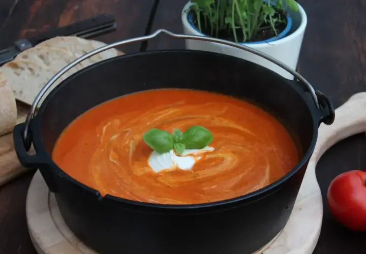 Ein köstliches Tomatensuppe Rezept mit frischen Tomaten, garniert mit Basilikum und einem Klecks Sahne, serviert in einem Gusseisentopf mit Brot.