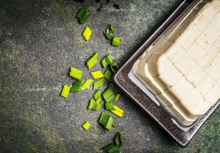 Seidentofu selber machen: Ein Block Seidentofu in einer Schale, daneben geschnittene Frühlingszwiebeln auf dunklem Untergrund.