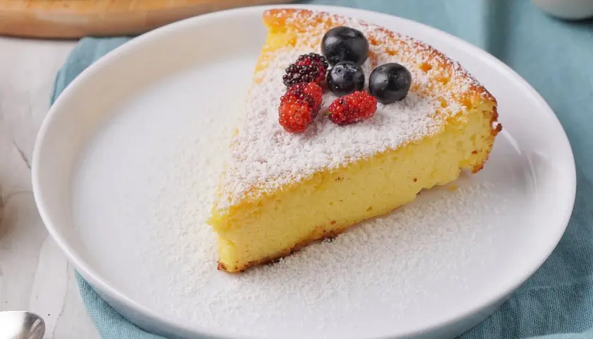 Ein Stück saftiger Quarkkuchen ohne Boden, bestäubt mit Puderzucker und garniert mit frischen Beeren.