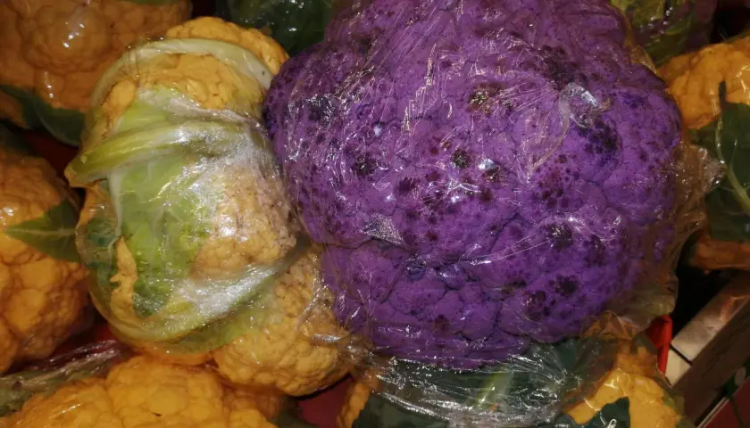Ein violetter Blumenkohl liegt verpackt zwischen gelben und grünen Blumenkohlen.